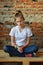 Young girl in jeans and white T-shirt is sitting on the floor and sad. Concept of a non happy teenager