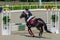 Young girl jumping with black horse. Blond pretty little girl going jump a hurdle in a competition.