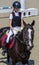 Young girl jumping with black horse. Blond pretty little girl going jump a hurdle in a competition.