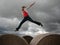 A young girl jumps from one hay bale to another on a cloudy day.