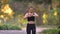 Young girl in jumpsuit with earphones running in autumnal park, stops to check the watch and continues jogging.