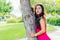 Young girl Latina brunette with long black hair and black eyes, wearing a red dress, looking at the camera leaning on a tree trunk