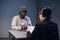 A young girl lawyer consults her client at the police station, a black guy in a cap and handcuffs.