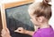 Young girl learning to write letters on blackboard