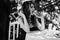 Young girl in a long evening dress is sitting at a white table in the park and eating a hamburger. Black and white photography