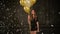 Young Girl with Long Hair in Short Dress Holds Gold and White Balloons, Silver Confetti Slowly Falling Down. Party Lady