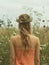 Young girl with long hair and a wreath of wild flowers on her head, walking in the green meadow. Midsummer. Generative AI