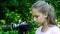 Young girl looks into video camera on background of green park background.