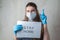 A young girl in a medical mask and gloves with an inscription on a sheet of paper calls for staying in quarantine at home. Home