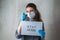 A young girl in a medical mask and gloves with an inscription on a sheet of paper calls for staying in quarantine at home. Home