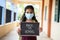 Young girl in medical mask holding back to school signage board at corridor - concept of school reopen, lifestyle and