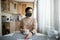 Young girl in medical mask looking out the window in the kitchen