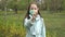 A young girl in a medical mask stands in the open air looking at the camera and waving a warning finger in front of the