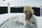 A young girl with a mug and a scraper cleans the car from snow. The girl cleans the car of snow