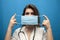 Young girl nurse puts on a viral mask on a blue background, protection of the coronavirus epidemic