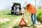 Young girl in orange vest set up breakdown triangle stands near a broken car