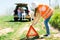 Young girl in orange vest set up breakdown triangle stands near a broken car