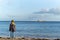 Young girl out of focus stood on beach looking out to sea in sunshine at big ocean liner oil tanker on the horizon