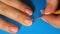 Young girl paints her nails with, makes a white stripe On a blue background in home. Make yourself a manicure.