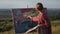 Young Girl Paints Picture In Nature. Female Artist Standing Near The Canvas With Brush In Her Hands.