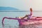 A young girl in a pink sundress resting in a small boat on calm water ,at sunset