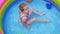 Young girl in pink swimsuit playing in colorful rainbow inflatable swimming pool backyard. Summer active lifestyle swim