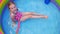 Young girl in pink swimsuit playing in colorful rainbow inflatable swimming pool backyard. Summer active lifestyle swim