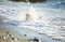 Young girl playing in breaking waves on beach. Big wave covering girl playing on sand