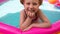Young girl playing in colorful rainbow inflatable swimming pool.Child in straw hat and pink swimsuit in clear blue water.