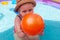 Young girl playing in colorful rainbow inflatable water swimming pool with orange ball. Happy child in straw hat smiling