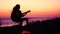 Young girl playing guitar on the beach with campfire at sunset