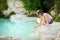 Young girl playing by natural swimming pool in Bagno Vignoni, with thermal spring water and waterfall. Tuscany, Italy