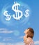 Young girl pointing at dollar sign clouds on blue sky