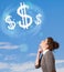 Young girl pointing at dollar sign clouds on blue sky