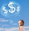 Young girl pointing at dollar sign clouds on blue sky