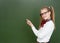 Young girl points on empty green chalkboard