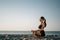 Young girl practices yoga on the ocean beach. Woman in lotus position on the sand. Meditation and relaxation at sea