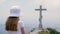 Young girl praying front orthodox cross monument on mountain peak. Tourist girl teenager standing on religious cross