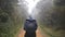 Young girl in raincoat going on wood trail during travel. Hiking woman with backpack walking in tropical wet forest