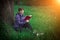 Young girl reading a book sitting on the grass near the oak at sunset. Summer vacation and camping. Fabulous beautiful composition