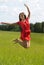 Young girl in a red dress jumping in a field coniferous forest