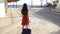 Young girl in red dress traveling on street with suitcase