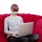 Young girl on red sofa working on laptop