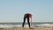 Young girl in red sportswear warming up on the beach. Stretching and cheerfulness in the morning.