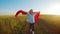 Young girl running with red tissue in green field. Happy cute girl playing in the wheat field on a warm summer day at