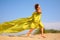 Young girl runs on sand in yellow fabric shawl