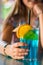 Young girl`s hand holding a glass with a blue lemonade cocktail with fruits