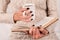 Young Girl\\\'s Hand with Stylish Black Nails Holds Book and Tea Cup, Woman in Wool Sweater Immersed in Reading