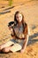 A young girl in safari style clothes sits on the golden sand with binoculars in her hands. Portrait