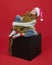 Young girl in a Santa hat is sitting on a black cube. photo session in the Studio on a red background